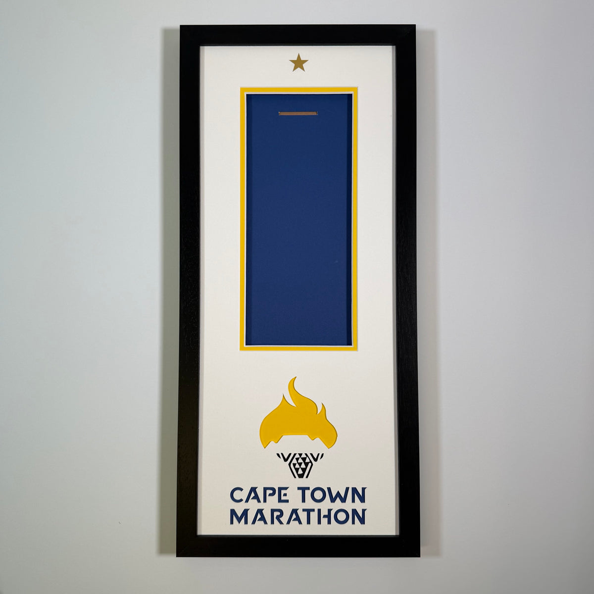Cape Town Marathon medal frame in black, with a yellow and blue inner mount, gold star, flame logo and lettering, by Phoenix Framers