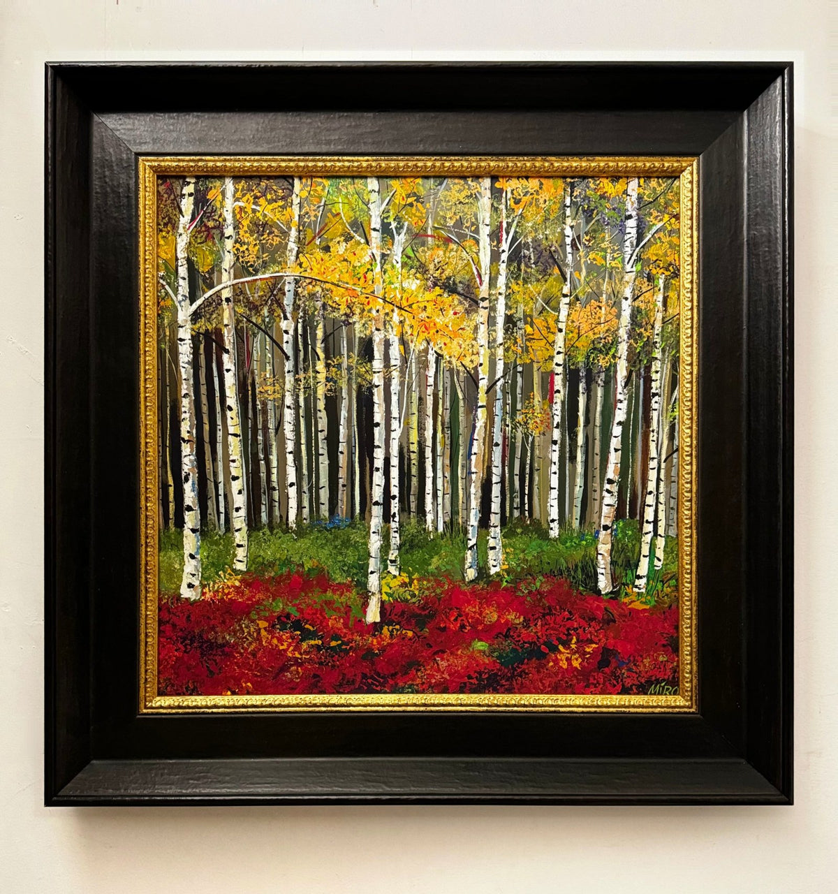 Painting of silver birch trees with golden leaves above a red forest floor, in a deep black frame with a gold inner edge.
